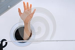 A man& x27;s hand sticks out of the porthole window on a ship at sea