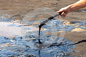 A man`s hand stirring liquid asphalt with a wooden stick at Pitch Lake, La Brea, Trinidad island, Trinidad and Tobago
