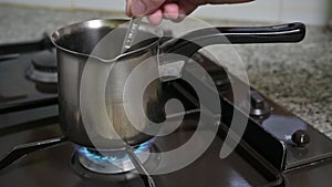 A man's hand stirs with a spoon inside a coffee warmer pan.