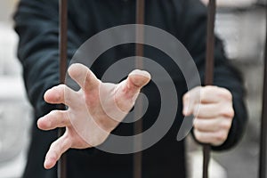 Man`s hand stretches through the bars locked man in a cage cell. Hand of a refugee behind fence