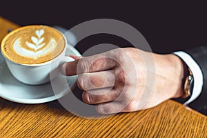 Man`s hand in a suit holding a cup of coffee