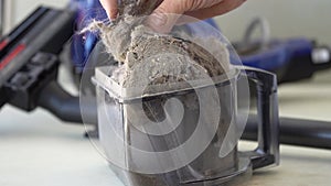 Man's hand takes dirt out of the vacuum cleaner container and shows it