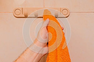 Man's hand takes an orange towel in the bathroom. Care and hygiene concept
