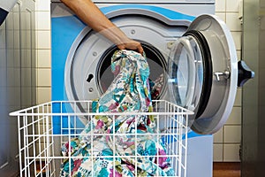 Man`s hand takes out the colorful laundry from the dryer and puts it in special basket on wheels. Laundry. Washer. Washing linen.