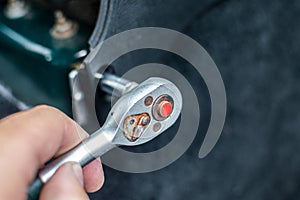 A man& x27;s hand tightens a bolt with a ratchet wrench. Selective focus, blurred background.