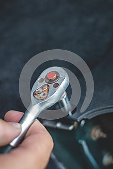 A man& x27;s hand tightens a bolt with a ratchet wrench. Selective focus, blurred background. Vertical view.