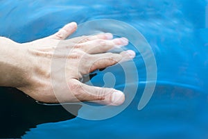 Man`s hand touches clean blue water photo
