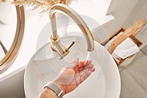 A man's hand touches the water in a beautiful sink with a golden faucet next to an oval mirror and a shelf with hand
