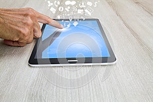 Man`s hand touching on tablet computer with world map, social and business icons on wooden desk