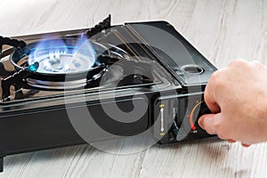 A man`s hand turns on a portable gas stove on a wooden table. An alternative source for cooking at home during a power outage