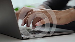 The man's hand is typing on a laptop computer keyboard at home or in the office. He is working, sending messages