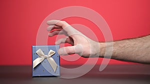 A man`s hand undulates toward the gift. Red background, close-up. Concept of holidays and gifts