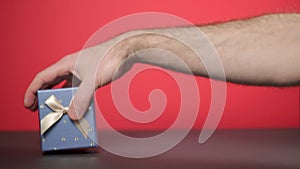 A man's hand undulates toward the gift. Red background, close-up. Concept of holidays and gifts