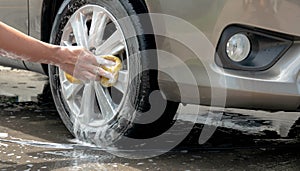 man`s hand using foam sponge to washing car wheel at home