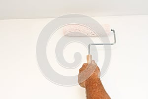 Man's hand using paint roller on white wall