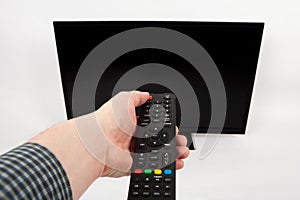 Man`s hand using remote control in front of the TV.