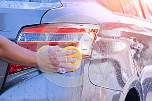 Man`s hand using sponge and foam to washing taillight modern car