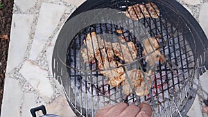 Man`s hand using tongs for turning chicken meat on the barbecue grill.