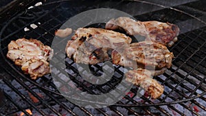 Man`s hand using tongs for turning chicken meat on the barbecue grill.