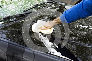 Man`s hand washes the car`s sponge mask with plenty of foam.