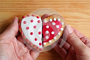 Man`s hand and woman`s hand holding two half heart shaped cookies attach