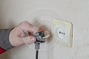 A man s hand in work clothes pulls an electric plug from a wall outlet