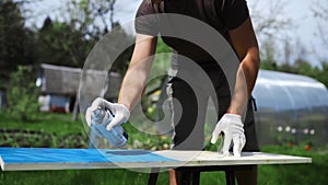 Man`s hand in working glove sprays paint with spray can to the wooden surface outdoors, man paints the DIY furniture at