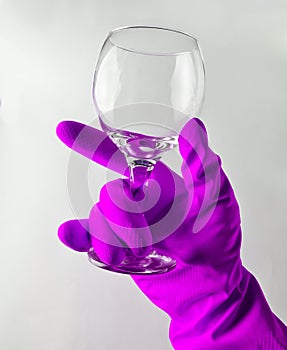 A man& x27;s hand in a yellow latex glove holds a clean glass wine gl