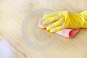 A man`s hand in a yellow rubber glove oil polishes the wooden surface of the table, the floor with a pink rag.