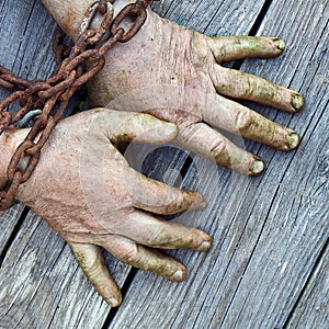 Man`s hands chained with old rusty thick chain on the wooden boards