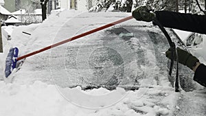 Man`s hands clearing snow of the front car window a long brush