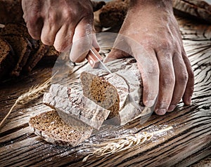 Man's hands cutting bread on the wood.