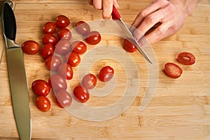 Man`s hands cutting fresh tomatos in the kitchen, preparing a meal for lunch. Topdown view.