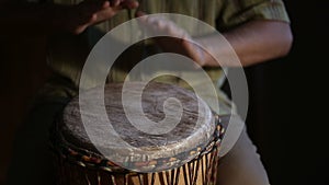 Man`s hands drumming out a beat on an African skin-covered hand drum.