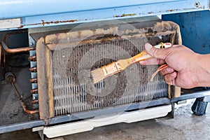 A man's hands held a brush to clean the dirty condensing unit
