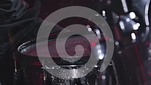 Man's hands hit the drums, creating a lot of splashes. A musician creates rock music on a drum kit in the rain in a dark