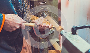 Man`s hands hold chisel near lathe, man working at small wood lathe, an artisan carves a piece of wood using a manual lathe