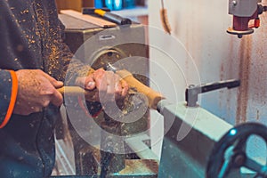 Man`s hands hold chisel near lathe, man working at small wood lathe, an artisan carves a piece of wood using a manual lathe