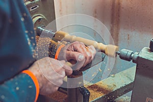 Man`s hands hold chisel near lathe, man working at small wood lathe, an artisan carves a piece of wood using a manual lathe