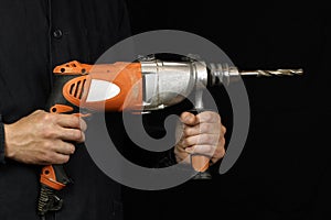 Man`s hands hold an electric drilling machine, drill on black background