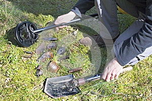 Man`s hands hold a metal detector and a shovel. The found militaria lie on moss and grass. photo