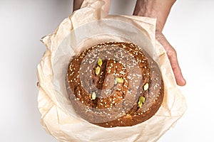 Man`s hands hold tasty fresh loaf of dark bread with sesame seeds on light background