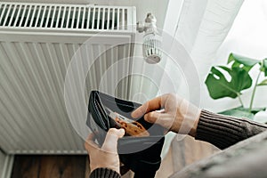 The man& x27;s hands hold a wallet with money next to the radiators. The concept of increasing prices for gas and energy