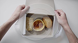 Man`s hands hold white plastic bag with white paper box with cake and buns.
