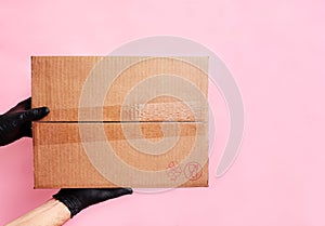 Man`s hands holding cardboard boxes in medical rubber gloves on pink background. Copy space. Online shopping and Express delivery