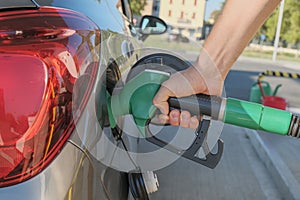 Man`s hands holding the gas pump and filling the car with fuel close-up across city streets. Energy industry. Gas station business