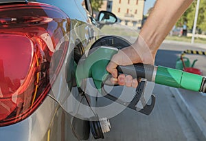 Man`s hands holding the gas pump, refueling his car with fuel close-up across city streets. Energy industry. Gas station business/