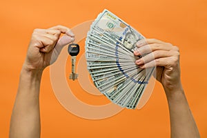 Man's hands holding keys and cash dollars isolated on orange background