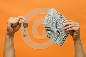 Man's hands holding keys and cash dollars isolated on orange background