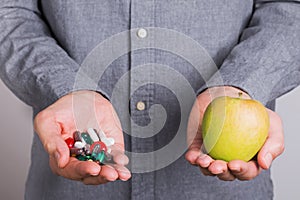 Man`s hands holding a ot of pills and capsules in one hand and apple in other.